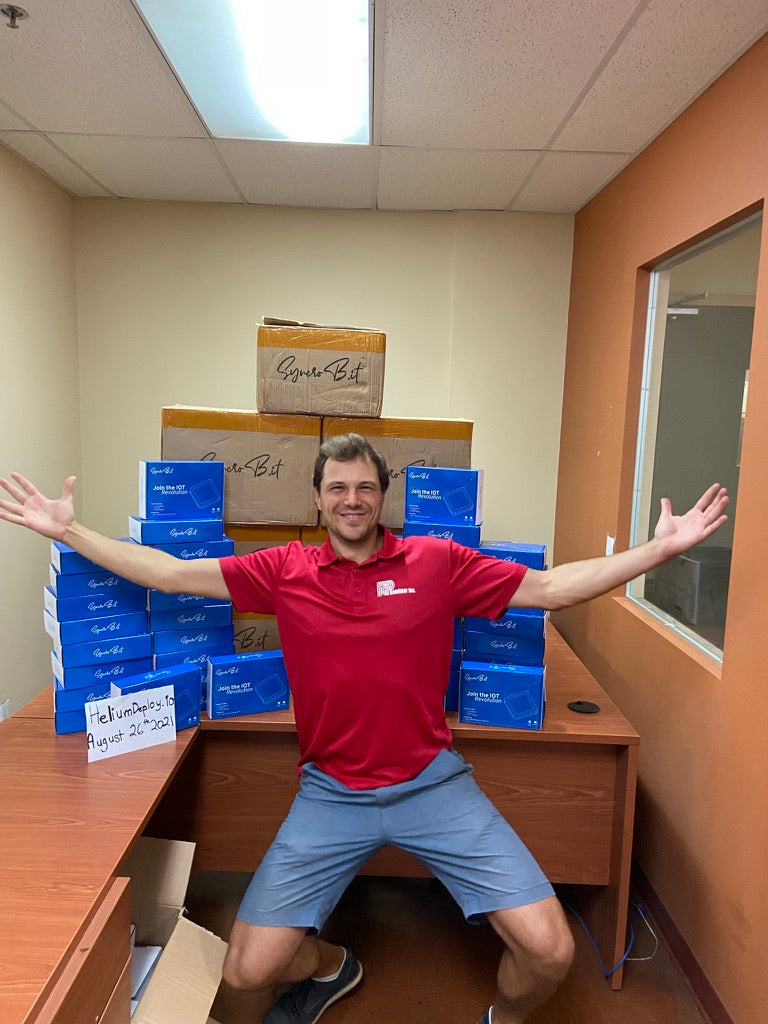 Founder in front of a stack of SyncroB.it Helium hotspot boxes — HeliumDeploy.io · August 26, 2021
